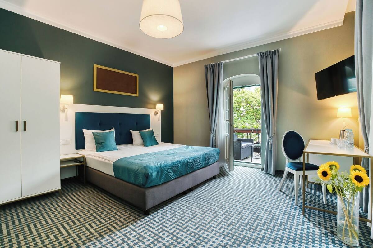 Habitación de hotel con cama, escritorio, silla, televisor y vistas al exterior.