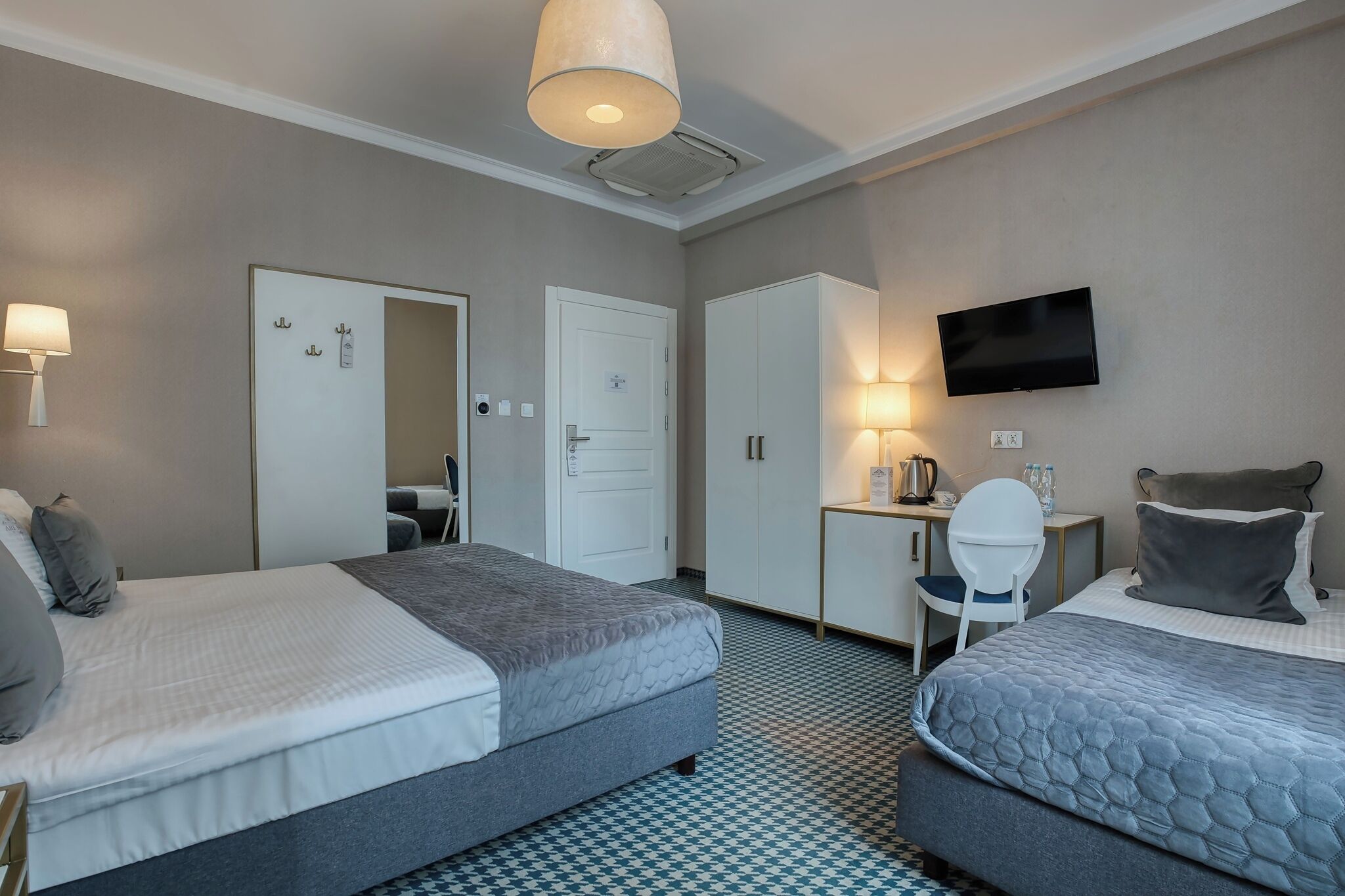 A hotel room with two beds, a desk, a chair, a TV, and a wardrobe.