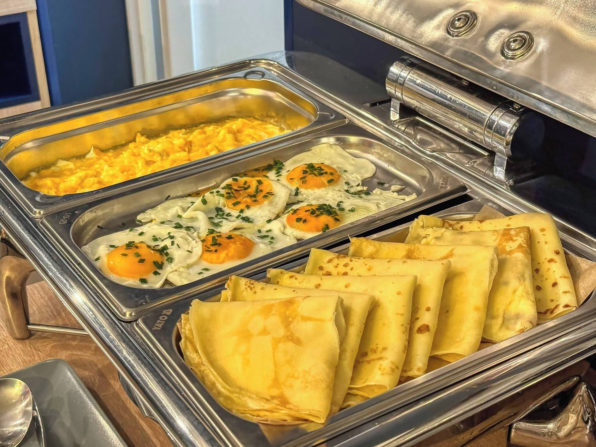 A buffet with scrambled eggs, fried eggs, and crepes.