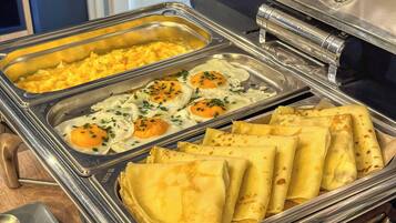 A buffet with scrambled eggs, fried eggs, and crepes.