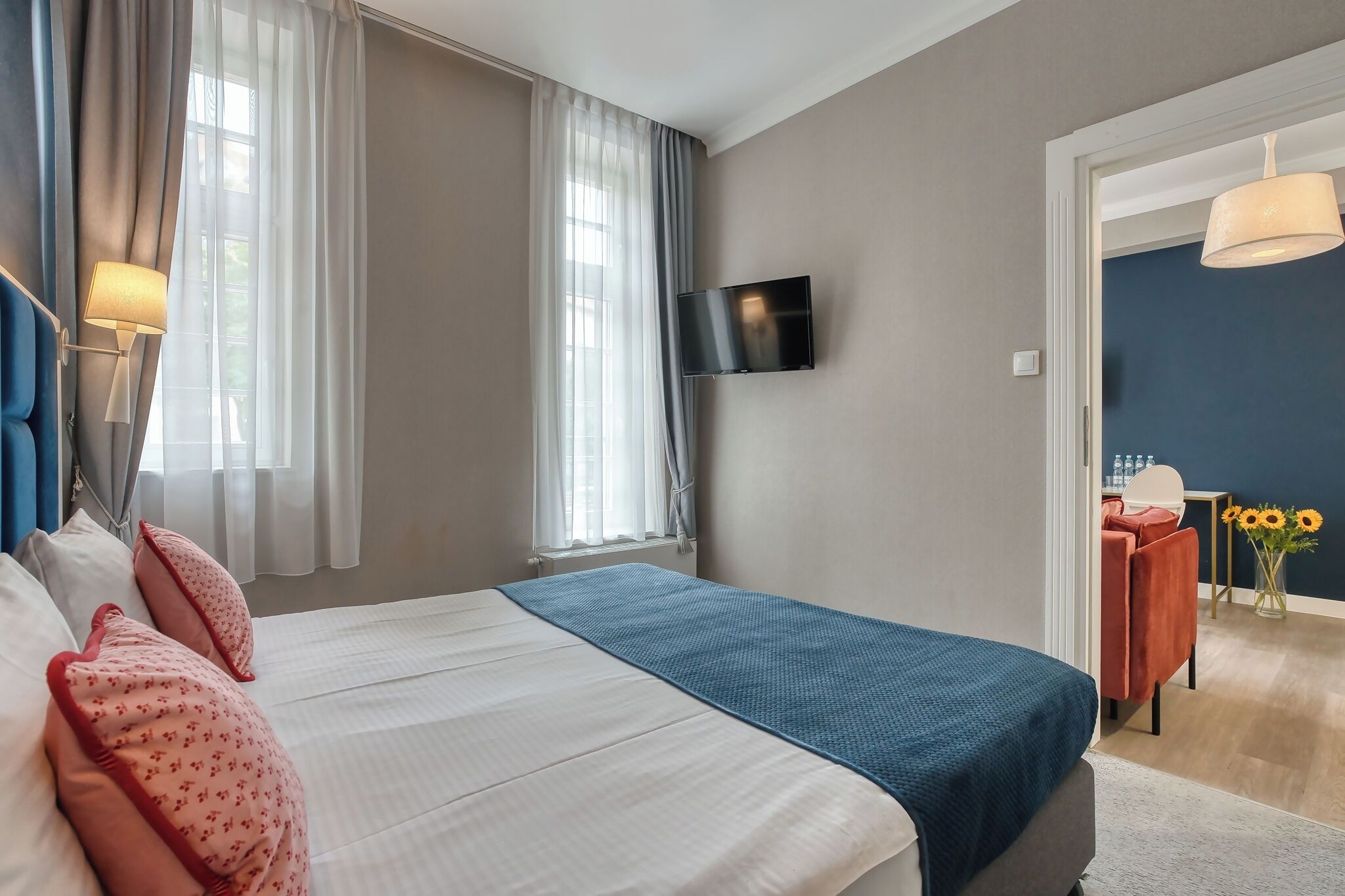 Un dormitorio con cama, cortinas, televisor y vistas a un comedor.
