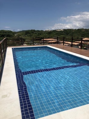 Uma piscina retangular com azulejos azuis e um deck de madeira ao redor.