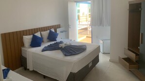 Ein Hotelzimmer mit Bett, Holz-Kopfteil, Klimaanlage in Weiß, einem kleinen Nachttisch und Blick ins Freie.