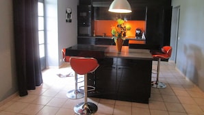 A modern kitchen with dark cabinetry, a central island with stools, and a hanging light fixture.