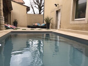 Uma piscina com superfície de água azul cristalina, rodeada por uma parede bege e um pilar de pedra.
