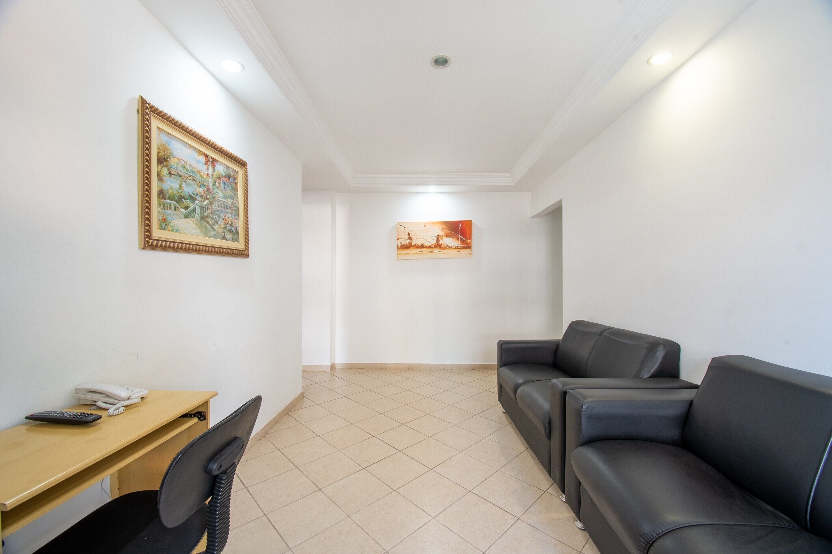 Une pièce comprenant un bureau, un canapé en cuir noir et deux tableaux accrochés aux murs.