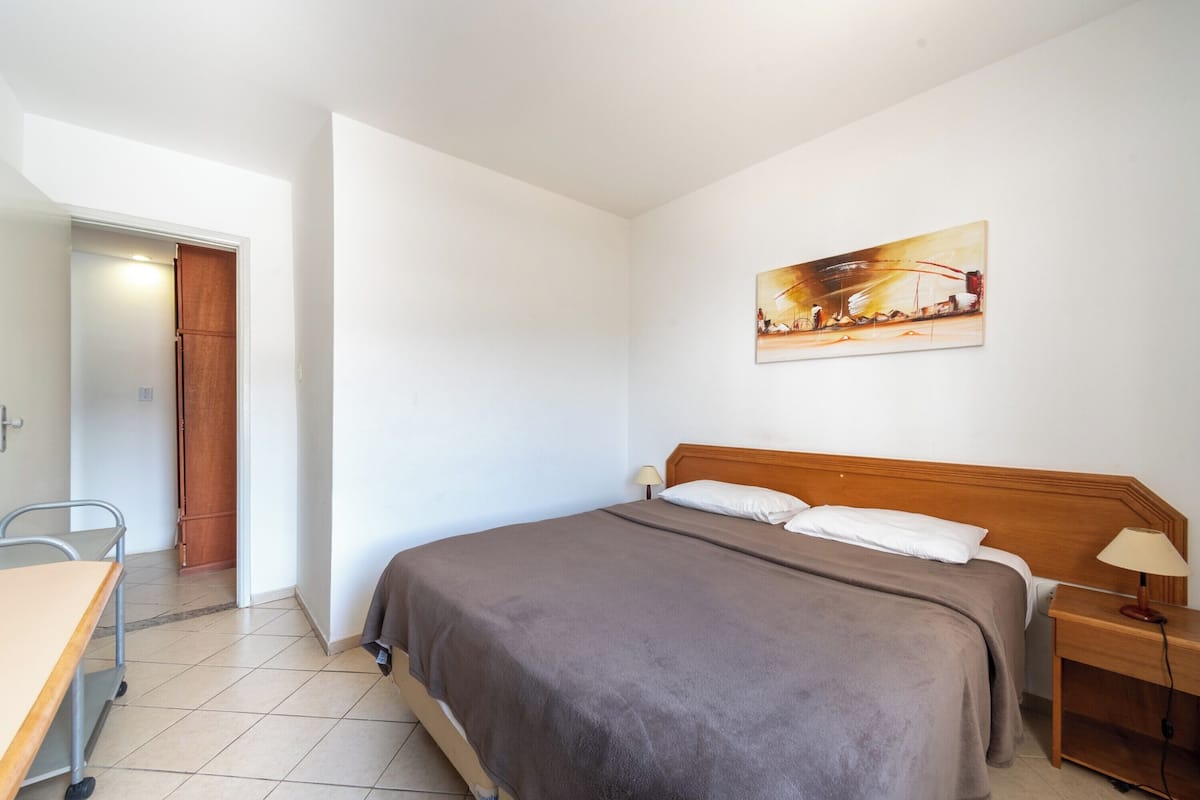 A bedroom with a bed, bedside table, and a painting on the wall.