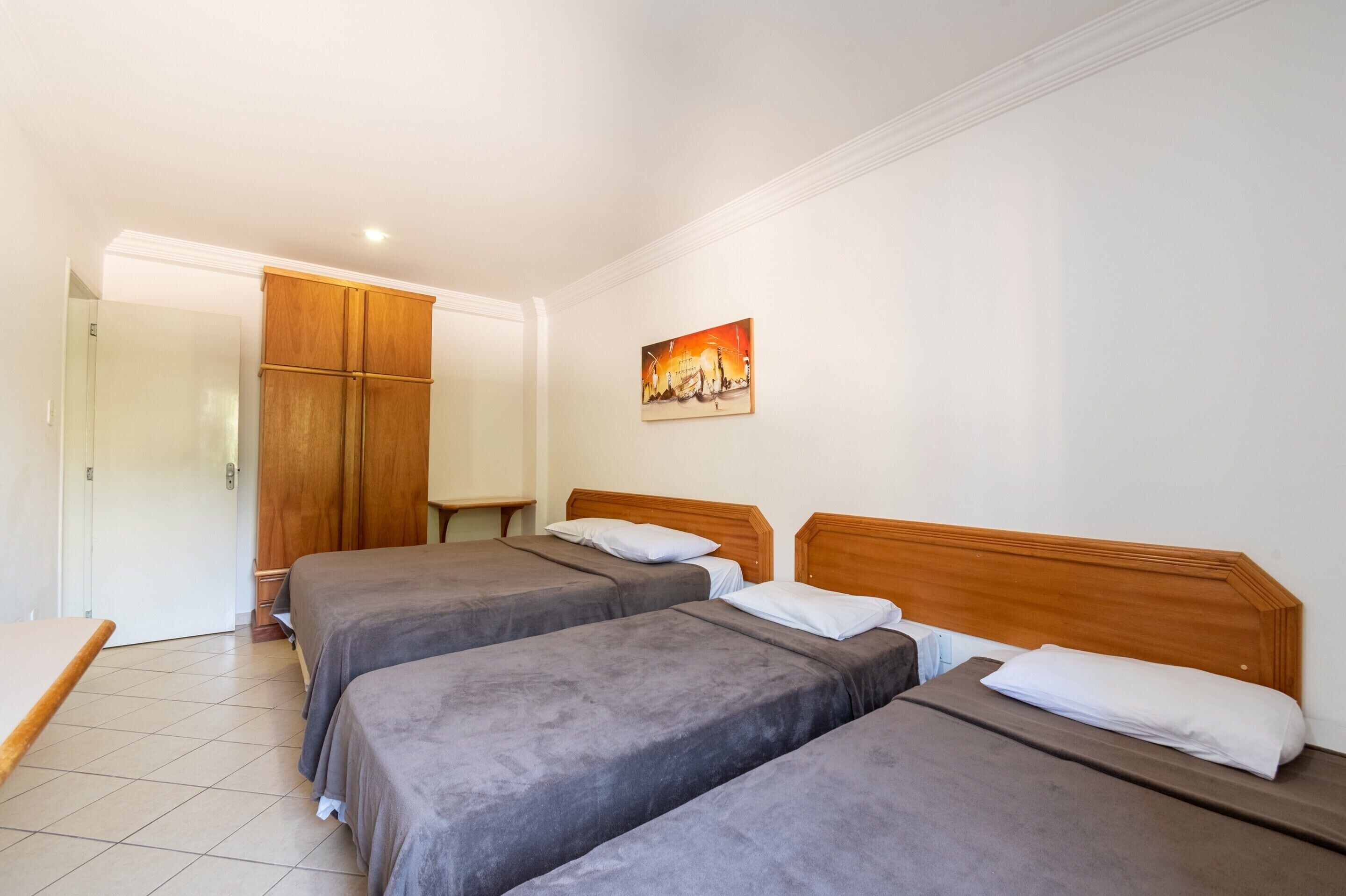 Habitación de hotel con dos camas, un armario de madera, una mesita pequeña y un cuadro en la pared.