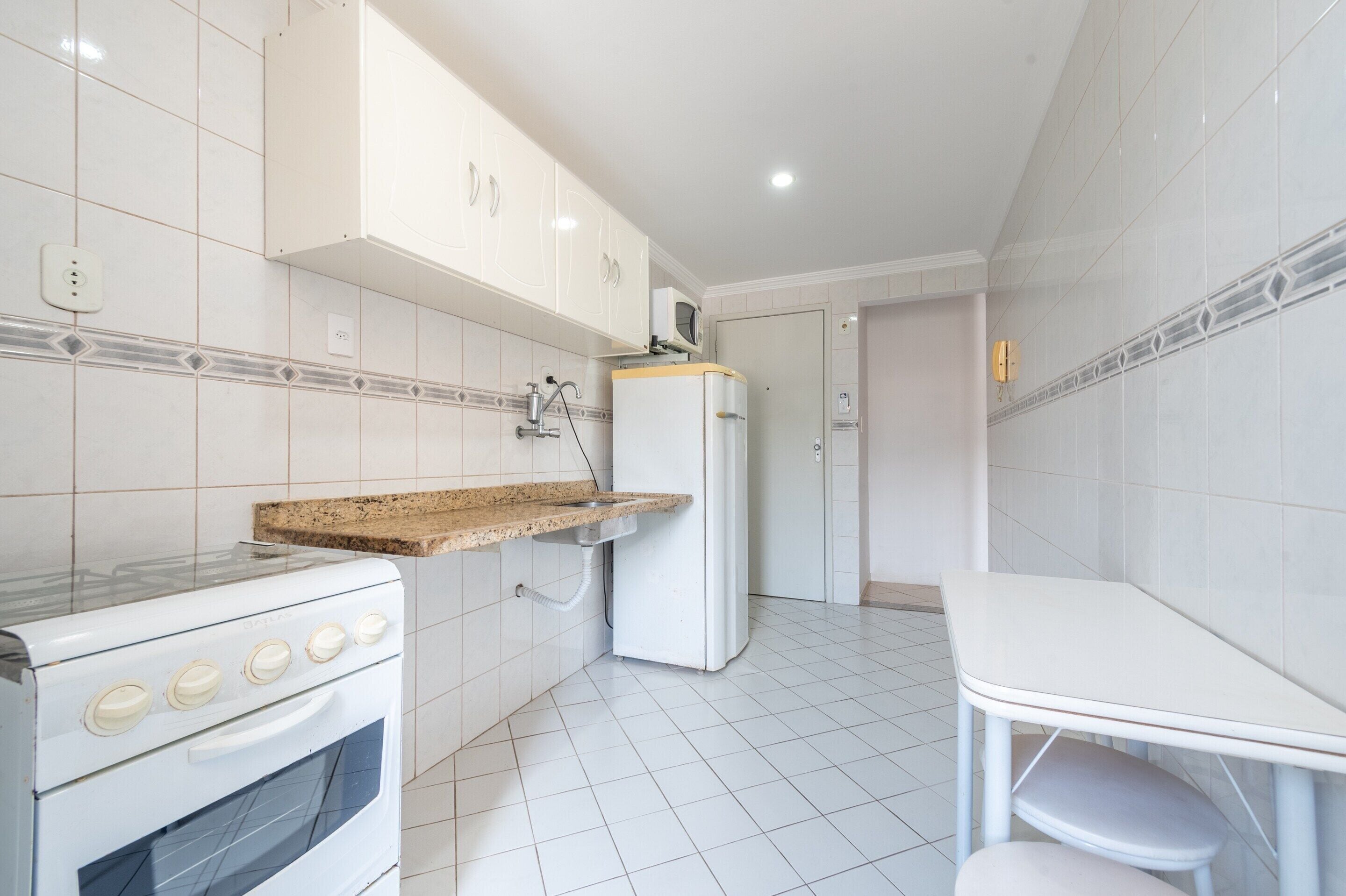 A kitchen with white cabinets, a microwave, a stove, a sink, and a small table.