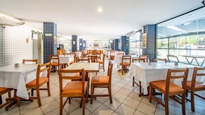 A spacious restaurant with multiple tables and chairs, large windows, and a tiled floor.