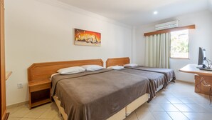 A hotel room with two beds, a desk, an air conditioning unit, and a painting on the wall.