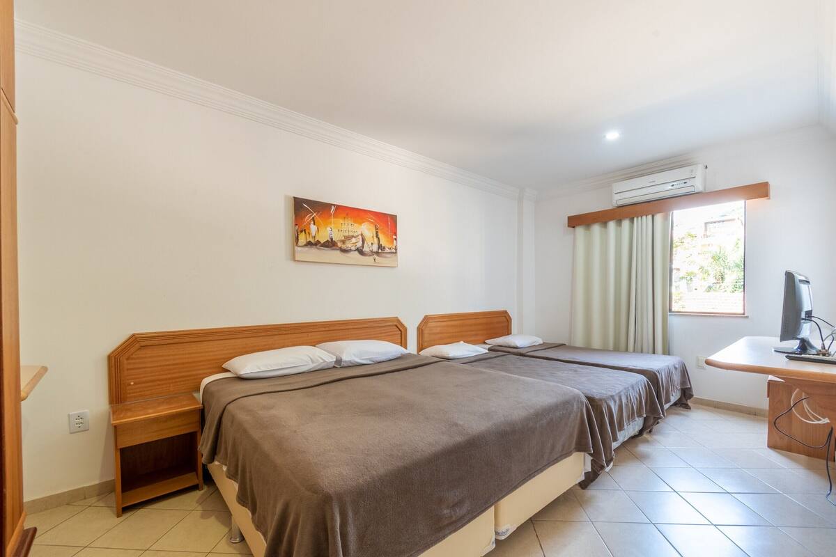 A hotel room with two beds, a desk, an air conditioning unit, and a painting on the wall.