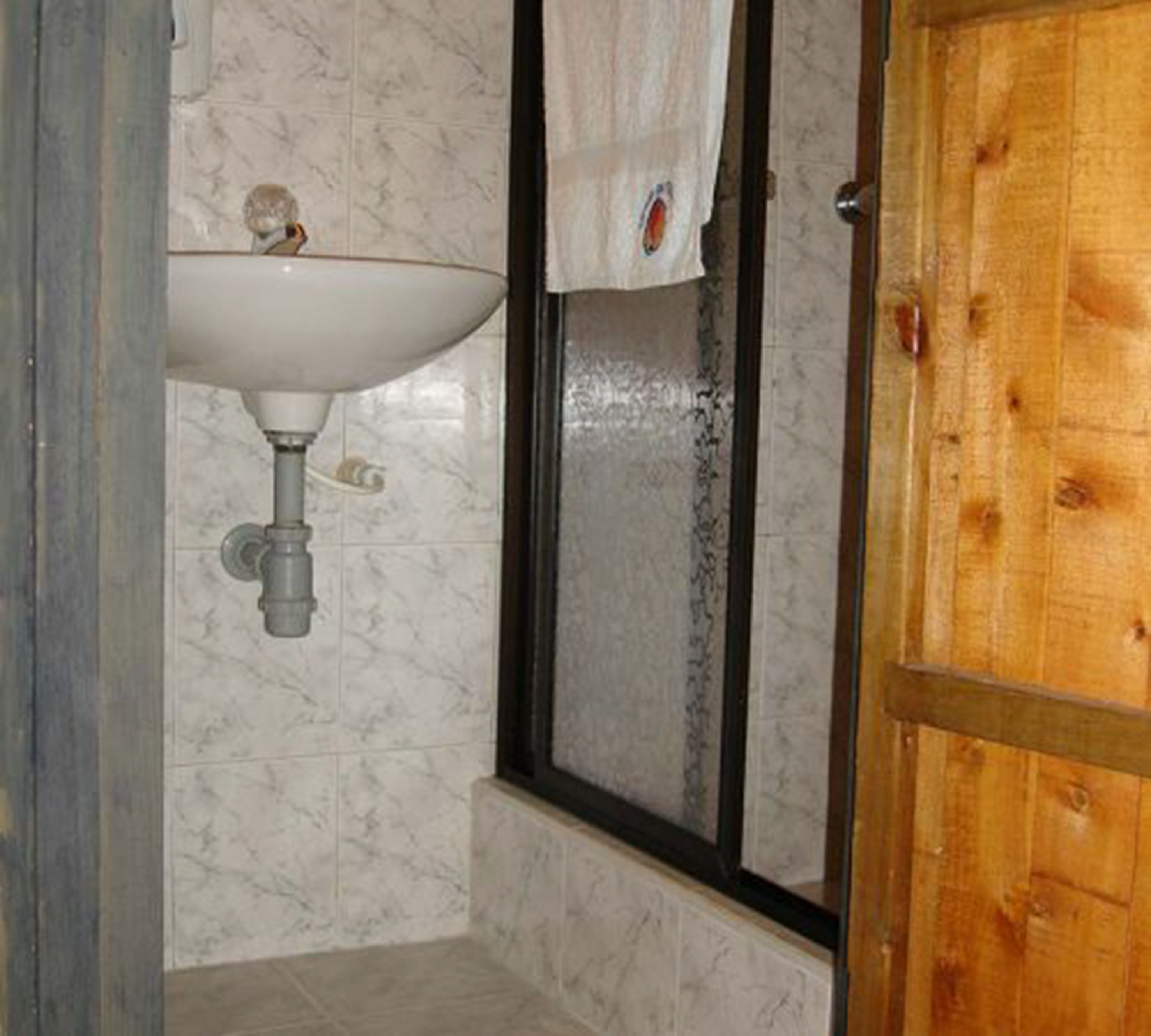 Un baño con lavamanos de mármol, puerta de madera y zona de ducha.