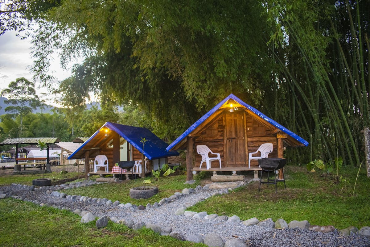 Deux cabanes en bois aux toits bleus, chacune équipée d’une chaise et d’une table.