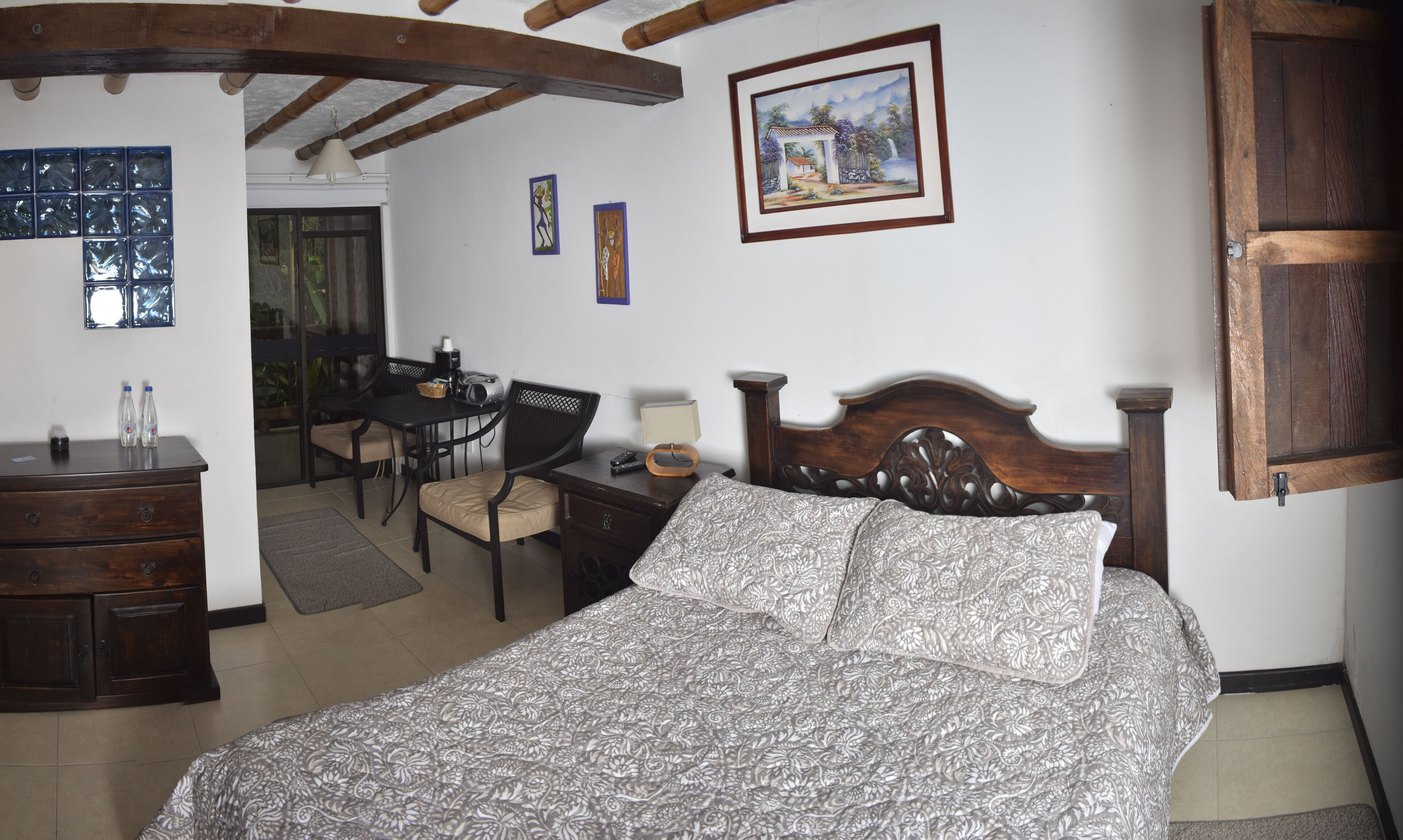 Un dormitorio con cama, cabecera de madera, un escritorio con sillas, una cafetera y un cuadro enmarcado en la pared.