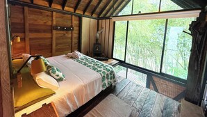 Um quarto aconchegante com cama, mesa de cabeceira, abajur e uma janela grande.