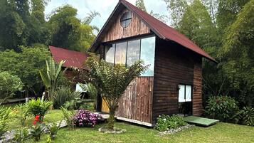 Una cabana de fusta amb una finestra gran i un teulat vermell, envoltada de vegetació exuberanta i un jardí ben cuidat.
