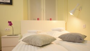 A neatly made bed with two pillows, a bedside table with a vase of flowers, and a wall-mounted lamp. - Elegant Apartament Copernicus (Warsaw)
