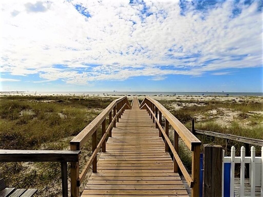 Ein hölzerner Steg führt zu einem Strand unter blauem Himmel.