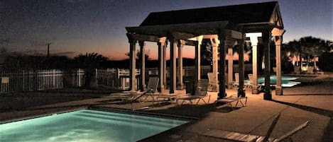 A covered pool area with lounge chairs and a gazebo structure.