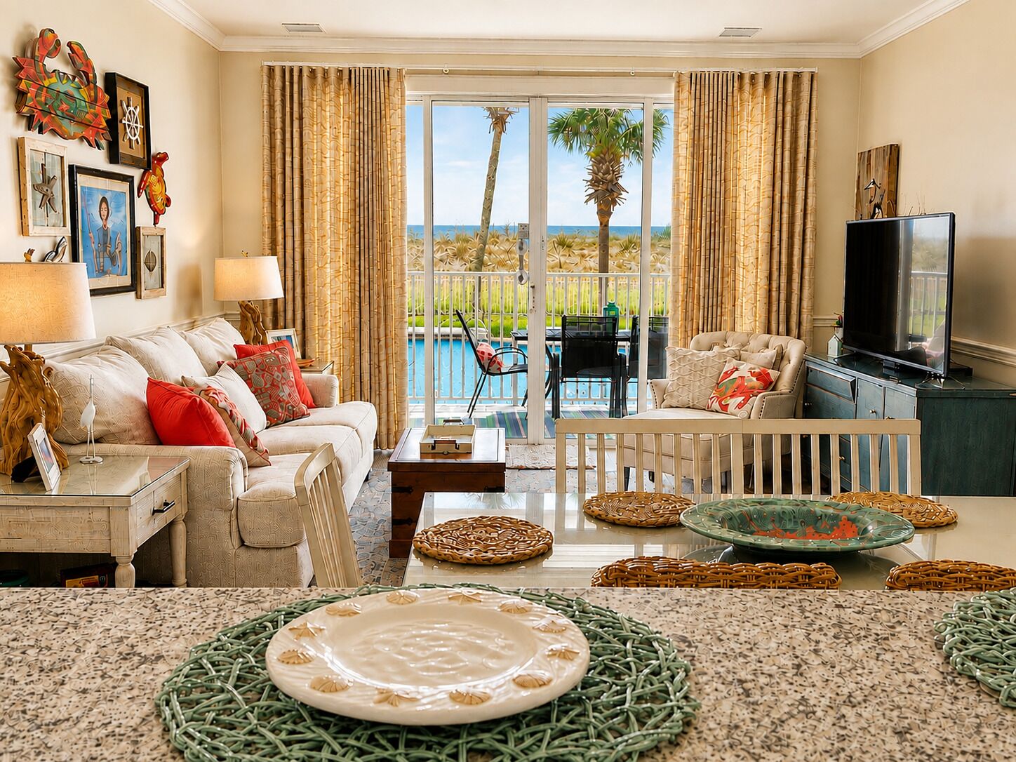 A living room with a view of the ocean, a television, and a dining area with a table and chairs.