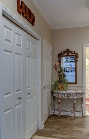A hallway with white double doors, a wooden 'Laundry' sign, a mirror with photos and a 'Thank you' message, and a small table with a plant. - 3bdrm/3bath- BEACHFRONT AND 5 steps to TWO POOLS - sleeps 8! (Dauphin Island)