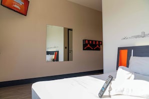 Quarto de hotel com cama, espelho, televisão presa à parede e cobre-leito.