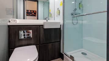 Un baño moderno con inodoro, lavamanos y ducha envuelta en cristal.