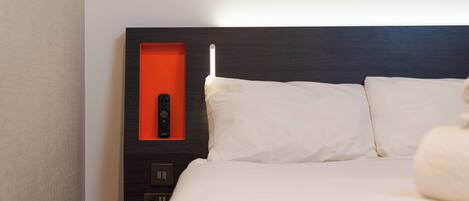Een hotelkamer met een bed, een afstandsbediening en een bedieningspaneel aan de muur.
