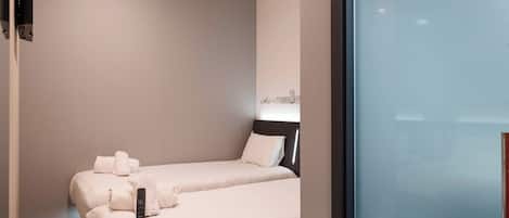 A hotel room with two beds, a flat-screen TV mounted on the wall, and a window with a view of a building.
