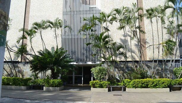 Un edificio moderno con fachada de rayas verticales, rodeado de palmeras y follaje.