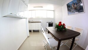 Una cocina compacta con armarios blancos, una mesa de comedor con sillas y un cuadro de un castillo en la pared.