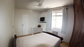 Un dormitorio con cama, escritorio, televisor y ventana con cortinas.