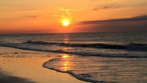 Um pôr do sol sobre o oceano, com ondas se aproximando da costa.