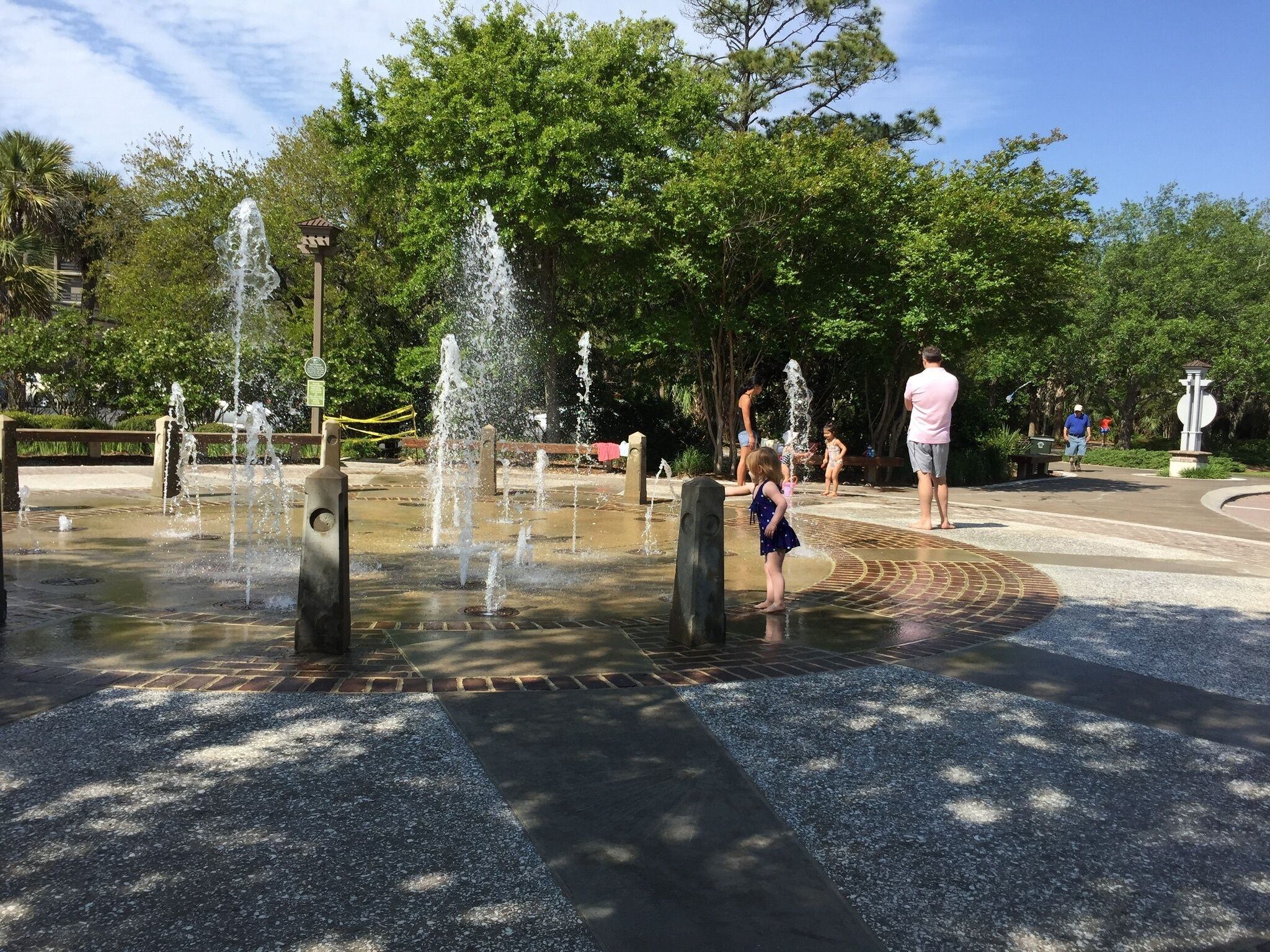 Ein öffentlicher Park mit einem Brunnenbereich, gepflasterten Wegen und Bäumen.