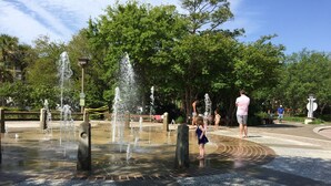 Um parque público com área de fontes, caminhos pavimentados e árvores.
