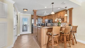Une cuisine avec des meubles de rangement en bois, un îlot central doté de tabourets, un ventilateur de plafond et un éclairage encastré.