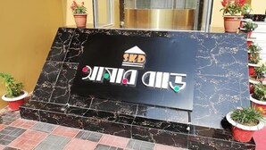 A sign with the text "SKD GOLD DINING" and a logo, placed on a black marble surface with a tiled floor around it. - SKD Amar Bari a Luxury Resort (Sreemangal)