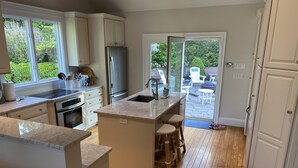 Cocina moderna con una isla central, suelo de madera y vistas al patio trasero a través de amplios ventanales.