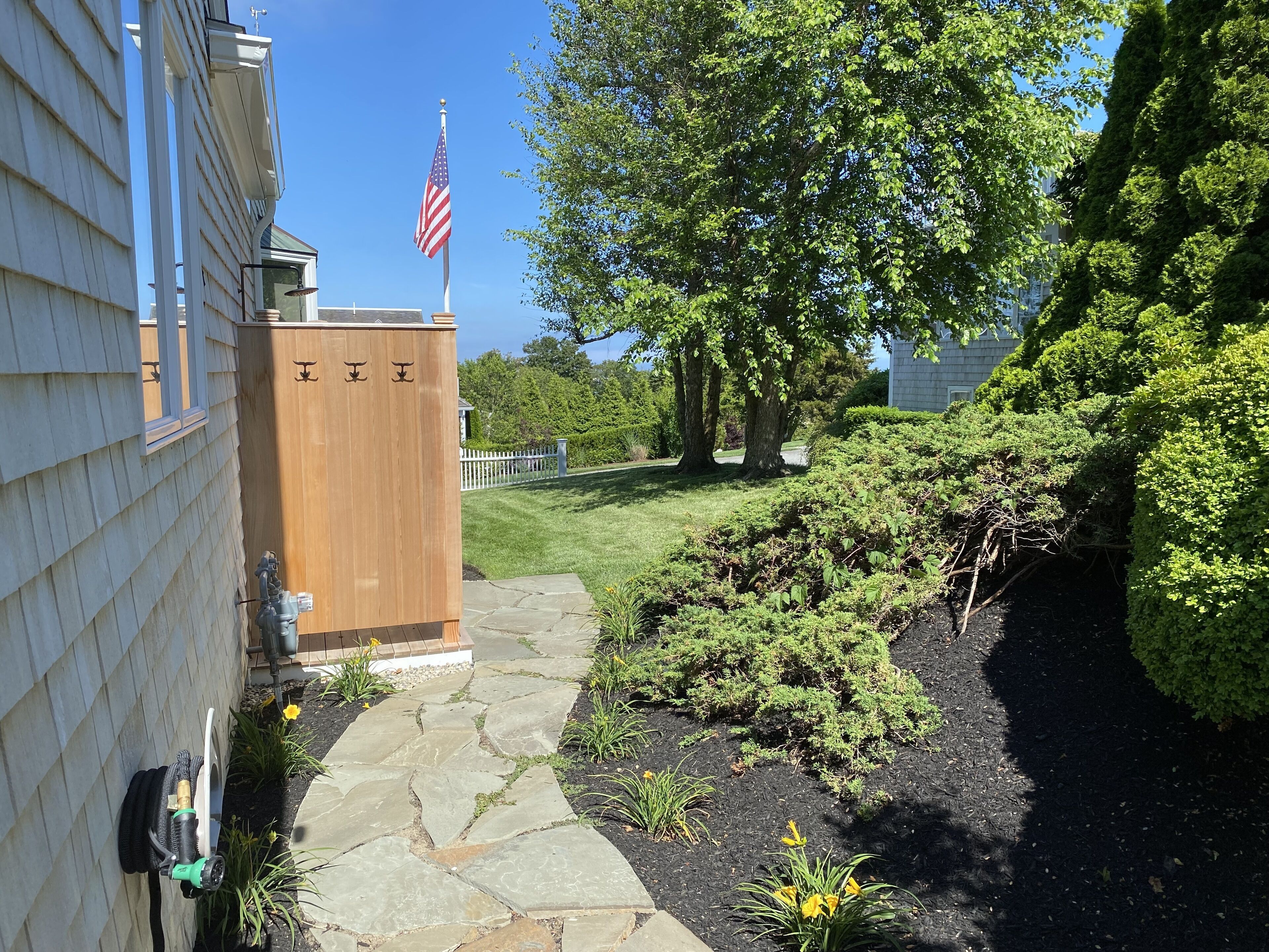 A stone pathway leading to a wooden structure with an American flag, surrounded by lush greenery and a well-maintained lawn.