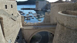 A historic stone bridge over a harbor with boats, a castle, and a hill in the background.