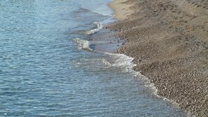 A beach with pebbles and sand, and waves gently lapping at the shore.