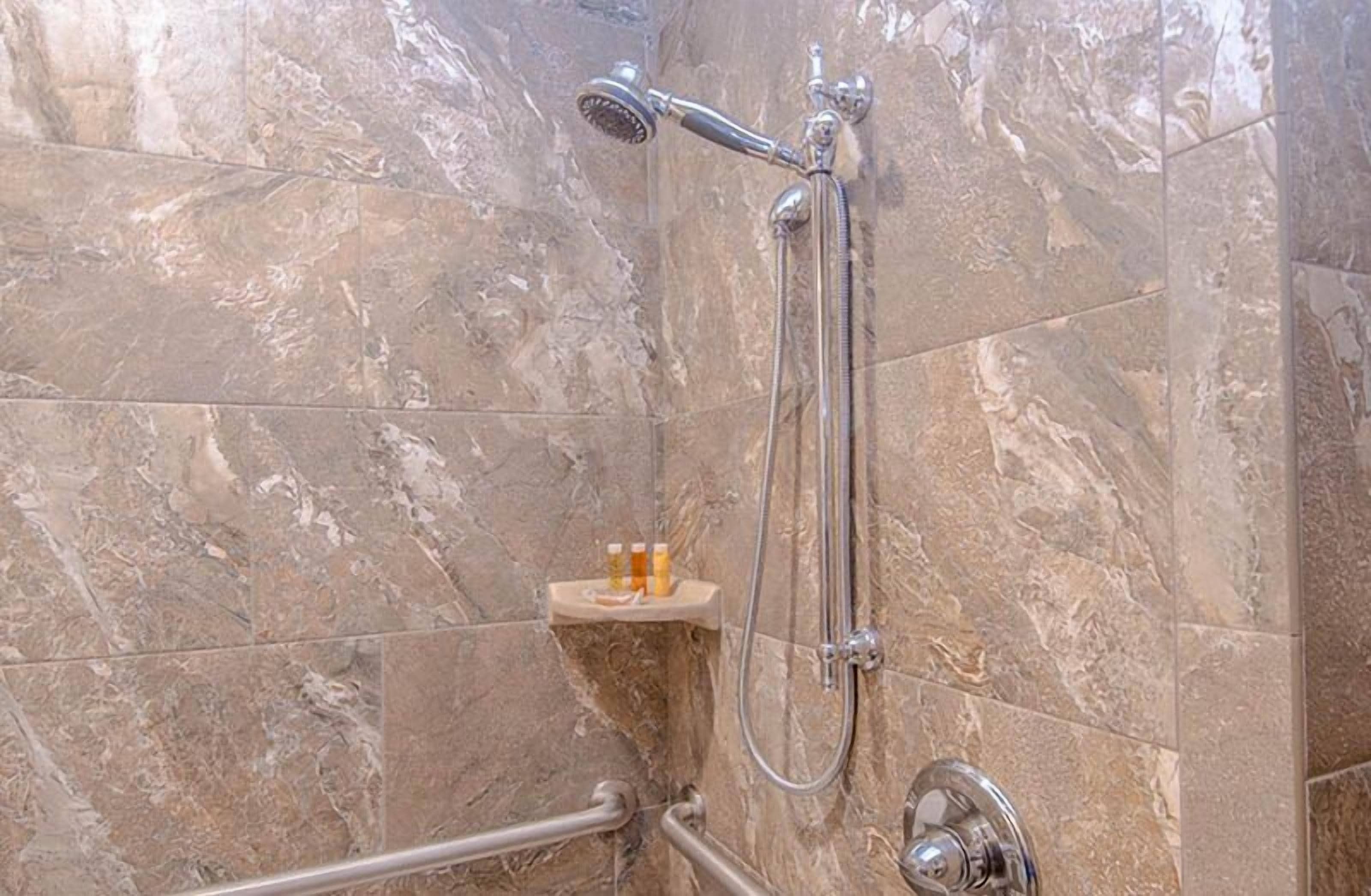 A bathroom with a shower, marble tiles, and a small shelf with bottles.