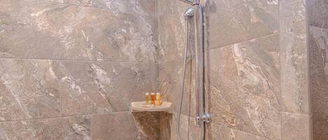 A bathroom with a shower, marble tiles, and a small shelf with bottles.