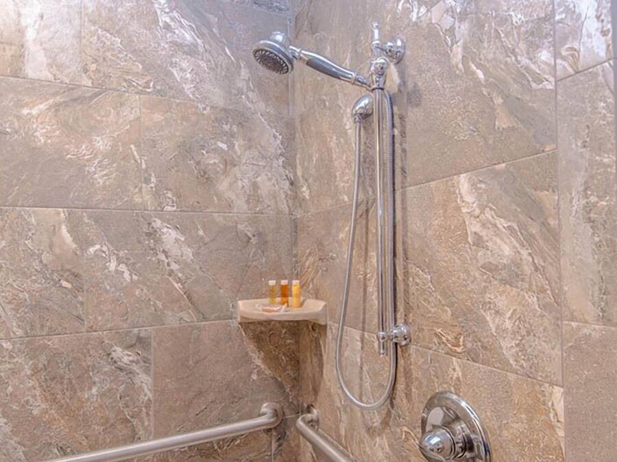 A bathroom with a shower, marble tiles, and a small shelf with bottles.