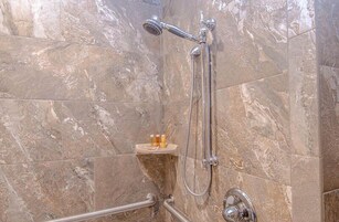 Un baño con ducha, baldosas de mármol y un pequeño estante con botellas.