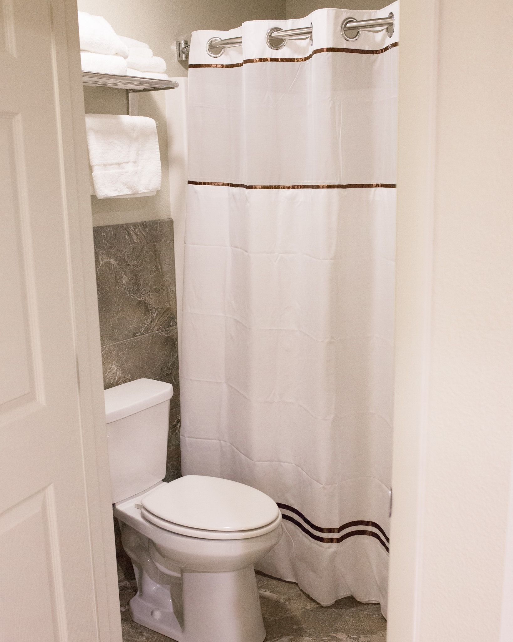 A bathroom with a toilet, a shower curtain, and a towel rack with folded towels.