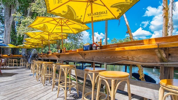 A wooden deck with yellow umbrellas, wicker chairs, and a bar area overlooking a body of water. - The Gator Den Motel (Dunnellon)