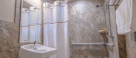 A bathroom with a sink, mirror, shower, and towel rack.