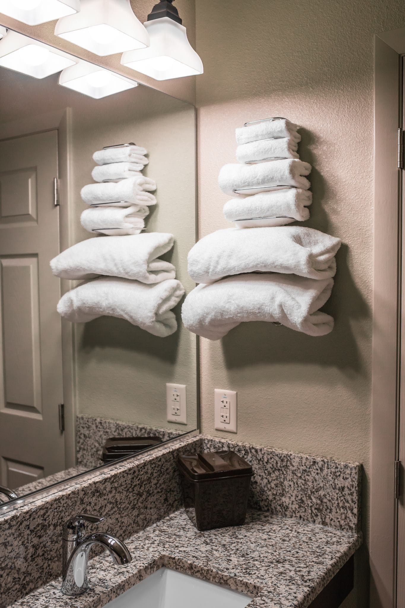 A bathroom with a granite countertop, a sink, a mirror, and two towel racks mounted on the wall.